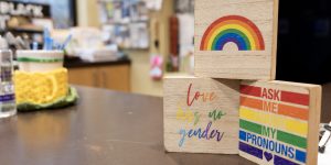 A set of 3 small wooden signs in rainbow colors with supportive LGBTQ+ messaging stacked in a pyramid on the check-in counter of a recovery support organization