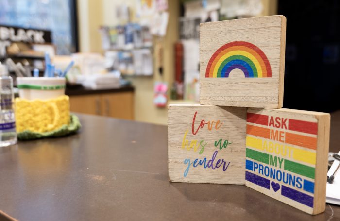 A set of 3 small wooden signs in rainbow colors with supportive LGBTQ+ messaging stacked in a pyramid on the check-in counter of a recovery support organization