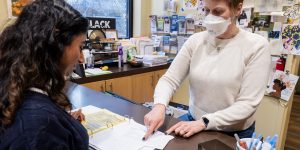 Person checking in at the front desk of a recovery support organization listens while a staff person points at a ledger and explains the process