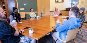 A diverse group of people sitting at a table listen while one person talks