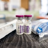 Two vials of intramuscular naloxone 0.4mg/mL sitting on a wooden table next to a packaged syringe and some other supplies.